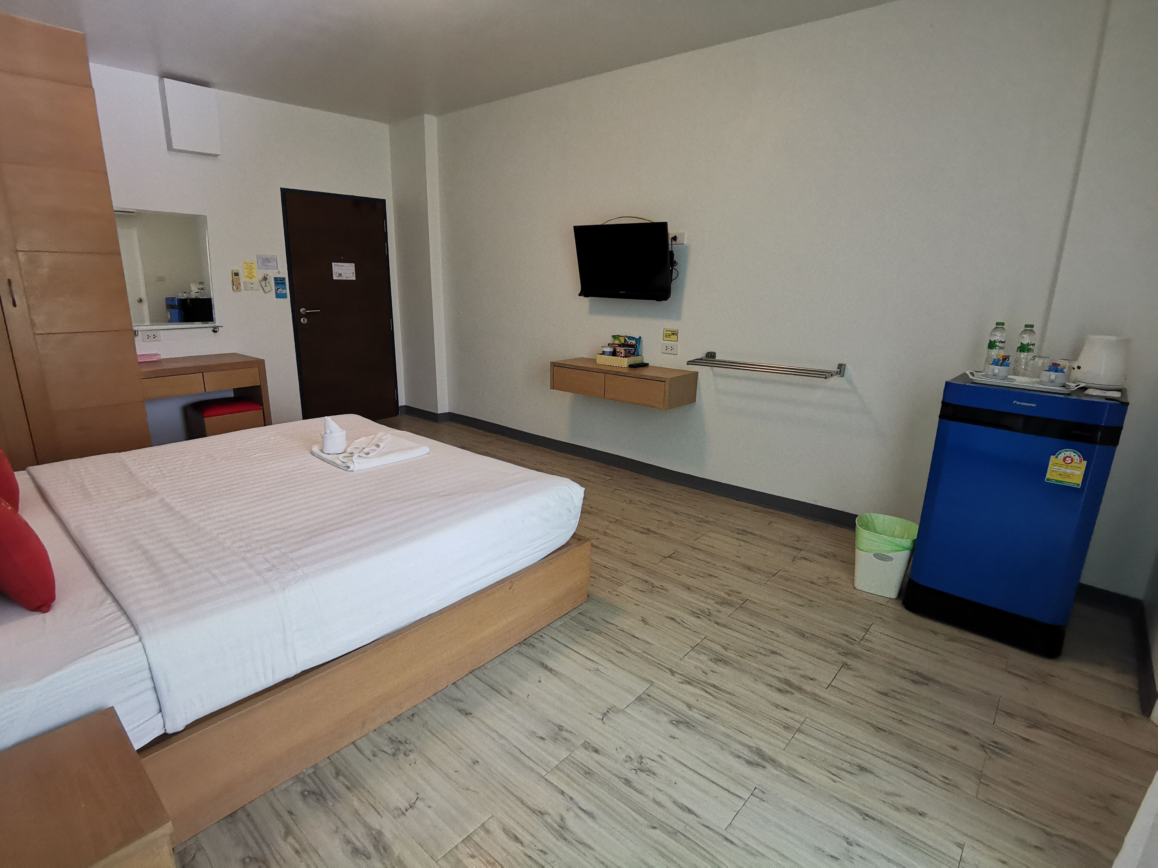 Ett hotellrum med en säng, ett skrivbord i trä, en spegel, en tv som är monterad på väggen, en minibar och en papperskorg.
