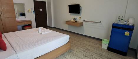 Ett hotellrum med en säng, ett skrivbord i trä, en spegel, en tv som är monterad på väggen, en minibar och en papperskorg.