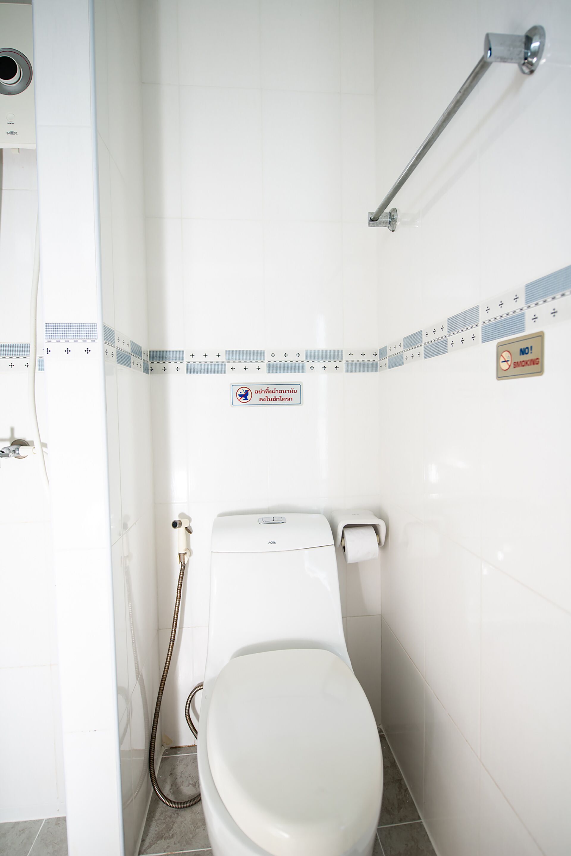 A small, clean bathroom with a toilet, a hand dryer, and a no-smoking sign on the wall.