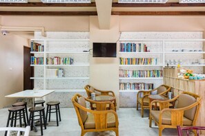 A cozy reading area with wicker chairs, a small table, and bookshelves filled with books. - Pure Phuket Residence (Phuket)