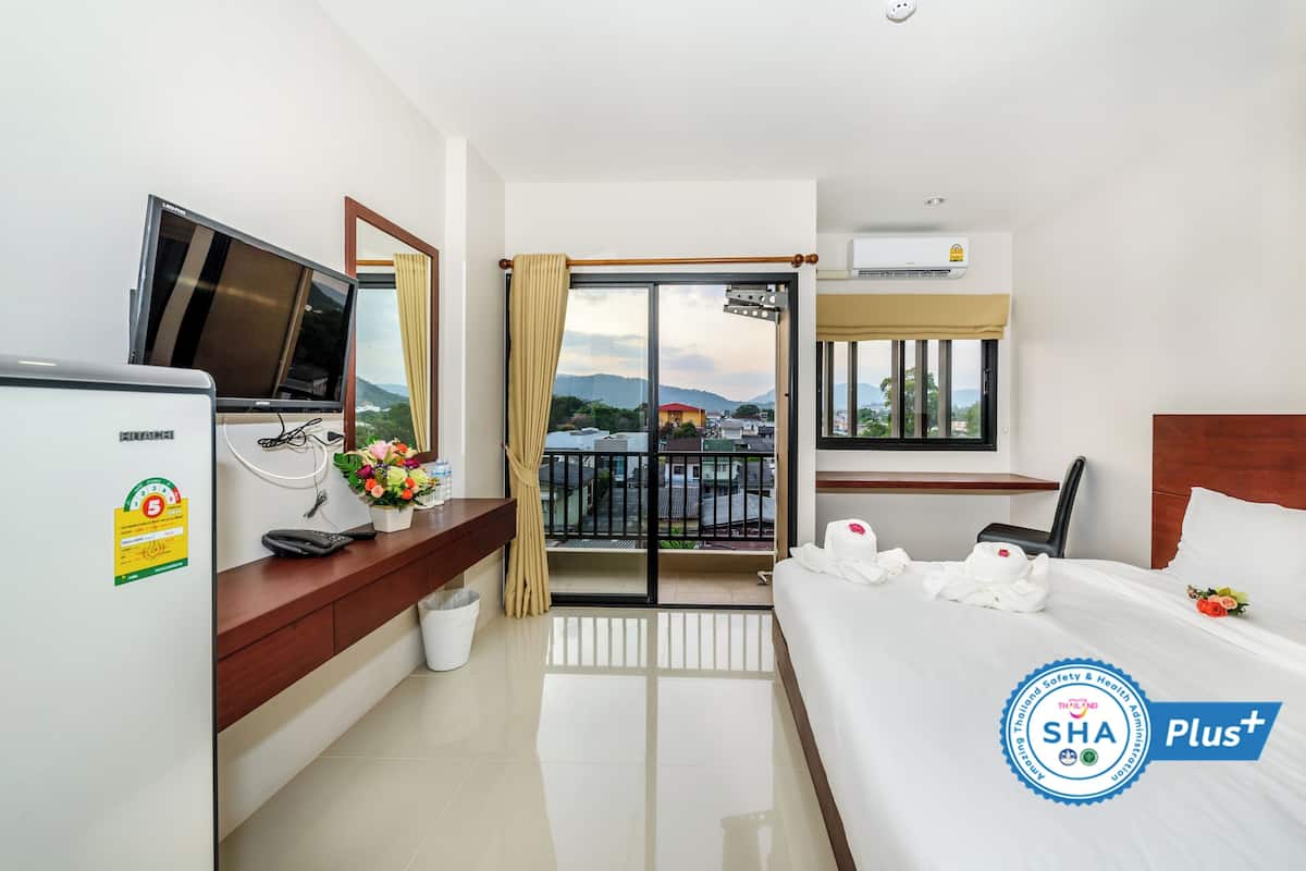 A hotel room with a bed, a desk with a TV, a window with curtains, a balcony, and an air conditioning unit.