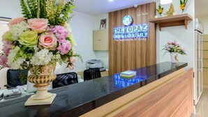 A reception desk with a wooden panel and a neon sign, a vase of flowers, and a printer. - The Topaz Residence (Phuket)