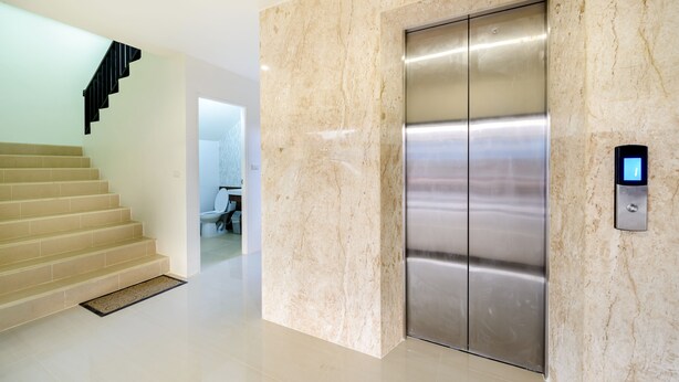 A modern elevator with a digital control panel, a marble wall, and a staircase leading to another room. - The Topaz Residence (Phuket)