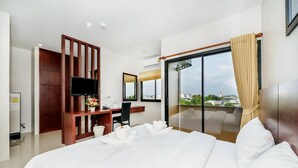 A modern hotel room with a large bed, a desk with a flat-screen TV, a wooden partition, and a balcony with a view. - The Topaz Residence (Phuket)