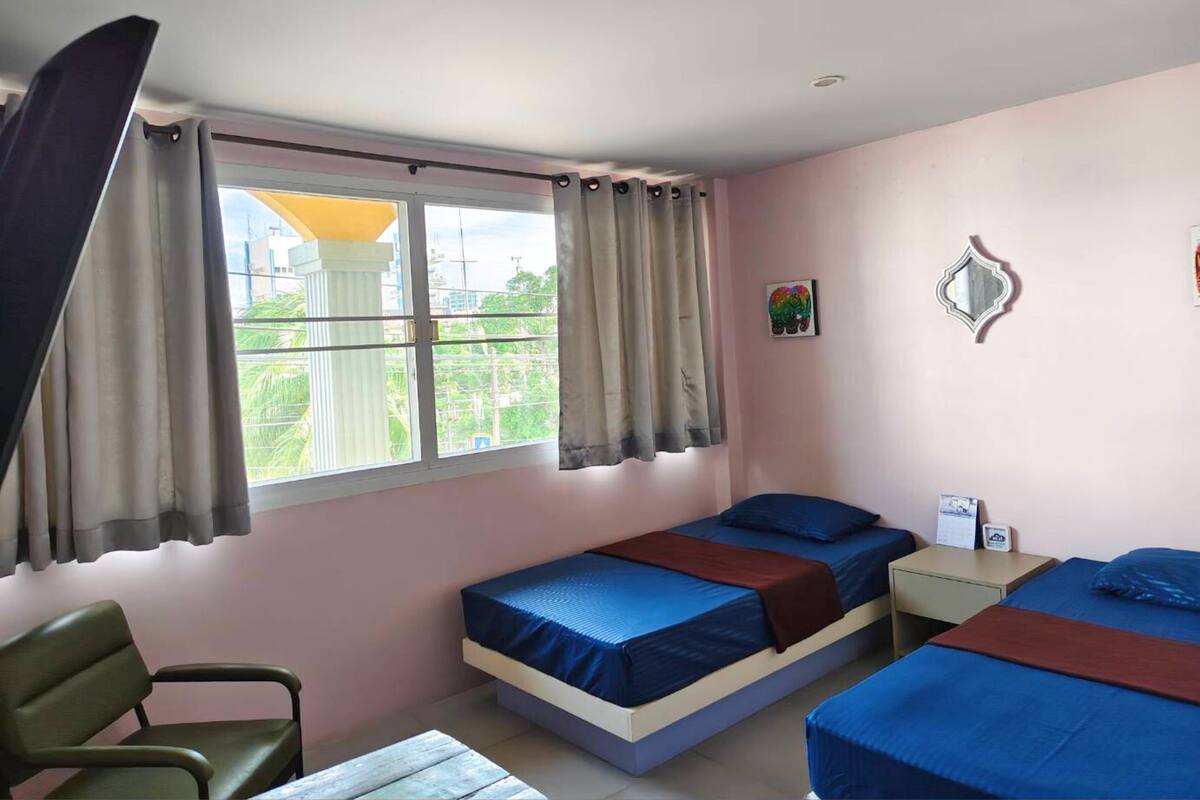 Un dormitorio con dos camas, una silla, una mesita y un ventanal con cortinas.