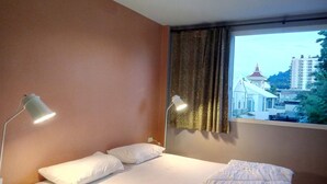 Une chambre d’hôtel avec un lit, deux lampes de chevet, une fenêtre avec des rideaux et une vue sur un immeuble doté d’une tour horloge.