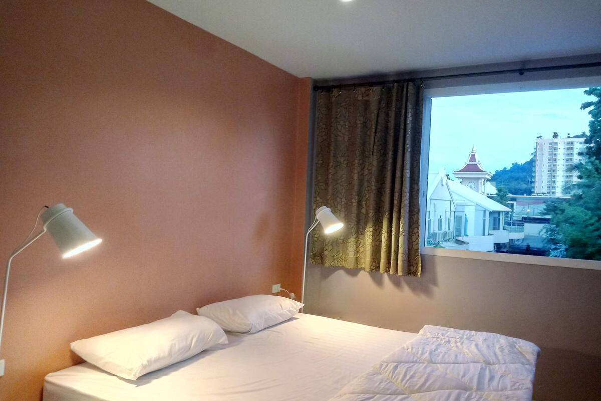 Habitación de hotel con una cama, dos lámparas de noche, una ventana con cortinas y vista a un edificio con una torre del reloj.