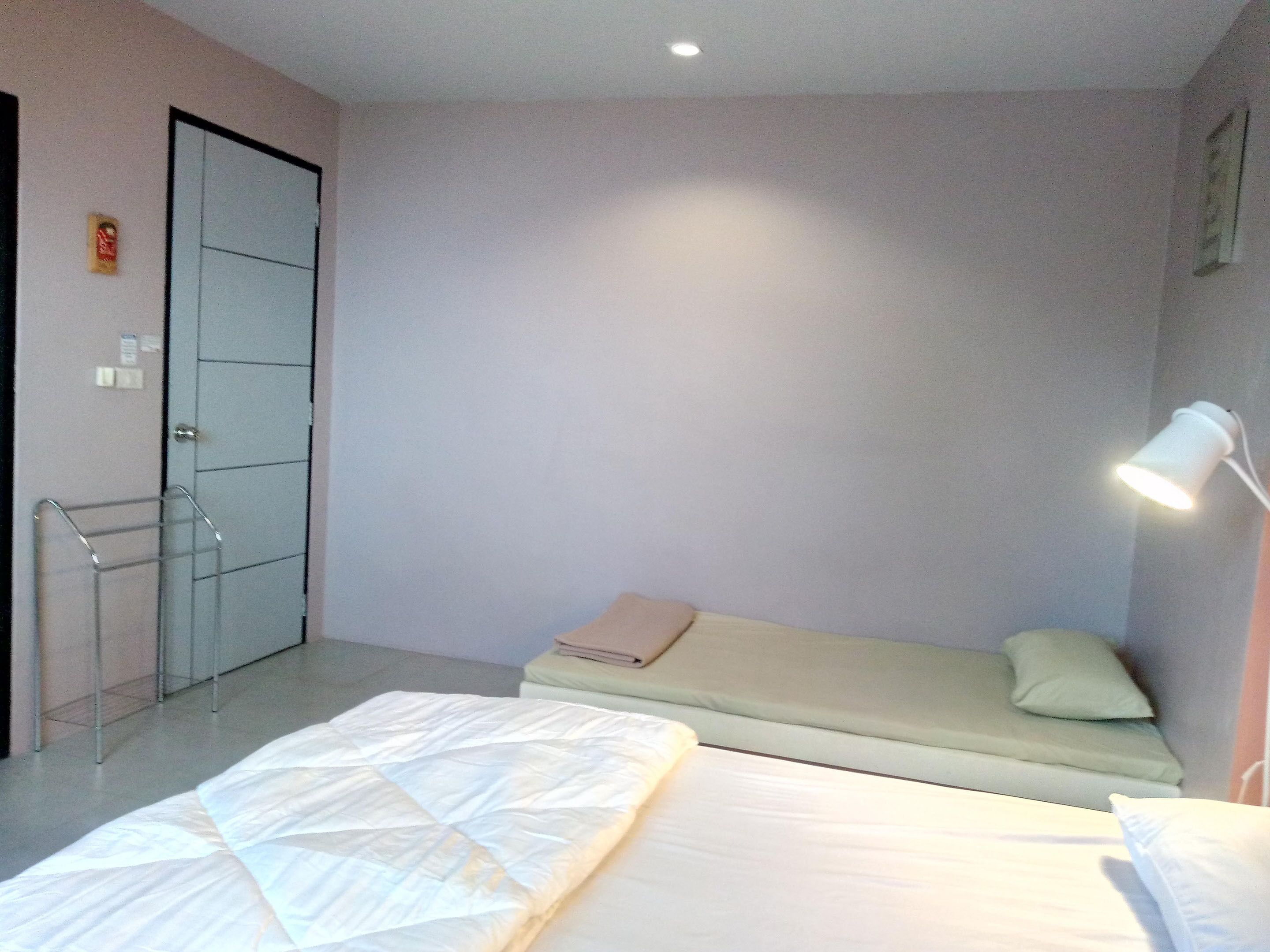 A hotel room with two beds, a bedside table, a lamp, and a door.