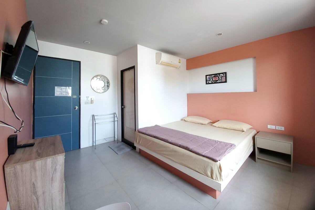 Un dormitorio con cama, escritorio, televisor, puerta y aire acondicionado instalado en la pared.