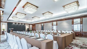 Een congreszaal met lange tafels, witte stoelen en kroonluchters.