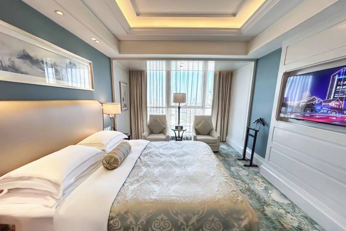 Une chambre d’hôtel avec un grand lit, deux fauteuils, une petite table et un téléviseur fixé au mur.