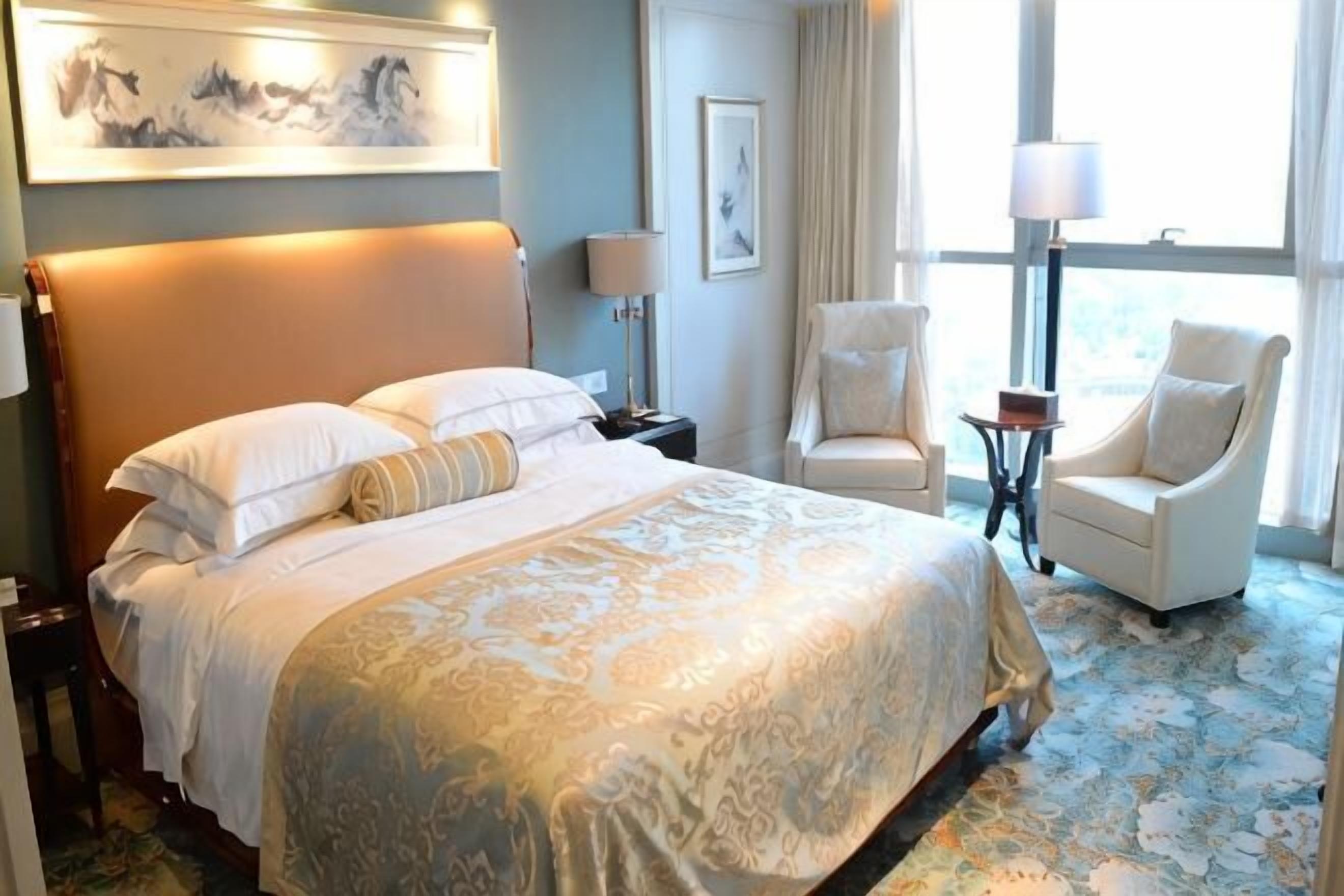 A hotel room with a large bed, two chairs, a small table, and a window with curtains.
