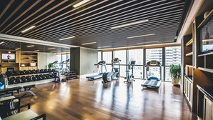 Een ruime fitnessruimte met houten vloeren, diverse fitnessapparaten en grote ramen met uitzicht op de stad.