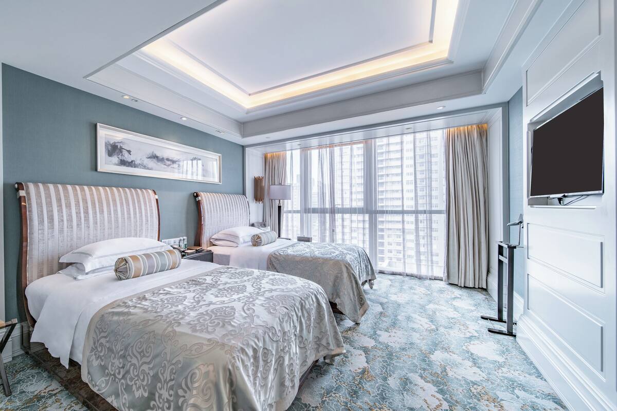 Une chambre d’hôtel avec deux lits, une grande fenêtre et un luminaire au plafond.