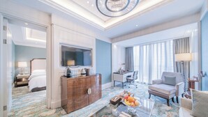 Une chambre d’hôtel avec un grand lit, un bureau, une chaise, une télévision et une table basse avec des fruits.