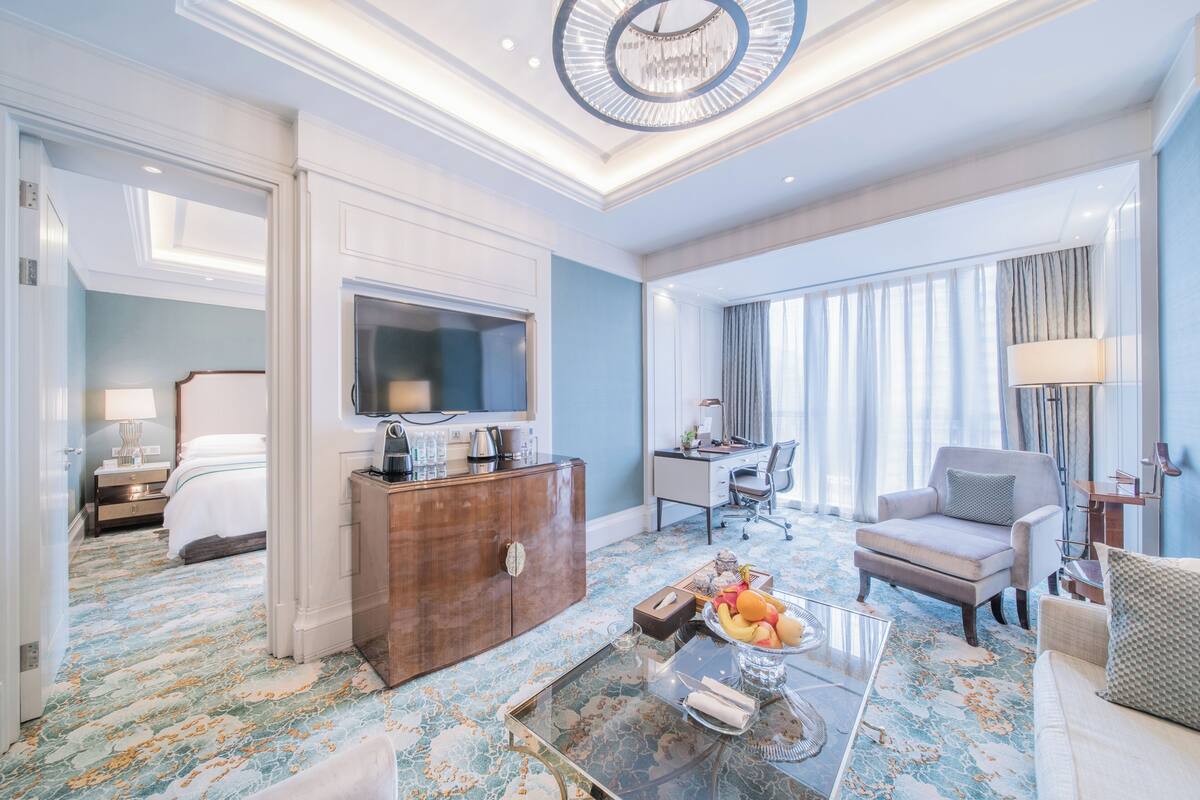 Une chambre d’hôtel avec un grand lit, un bureau, une chaise, une télévision et une table basse avec des fruits.