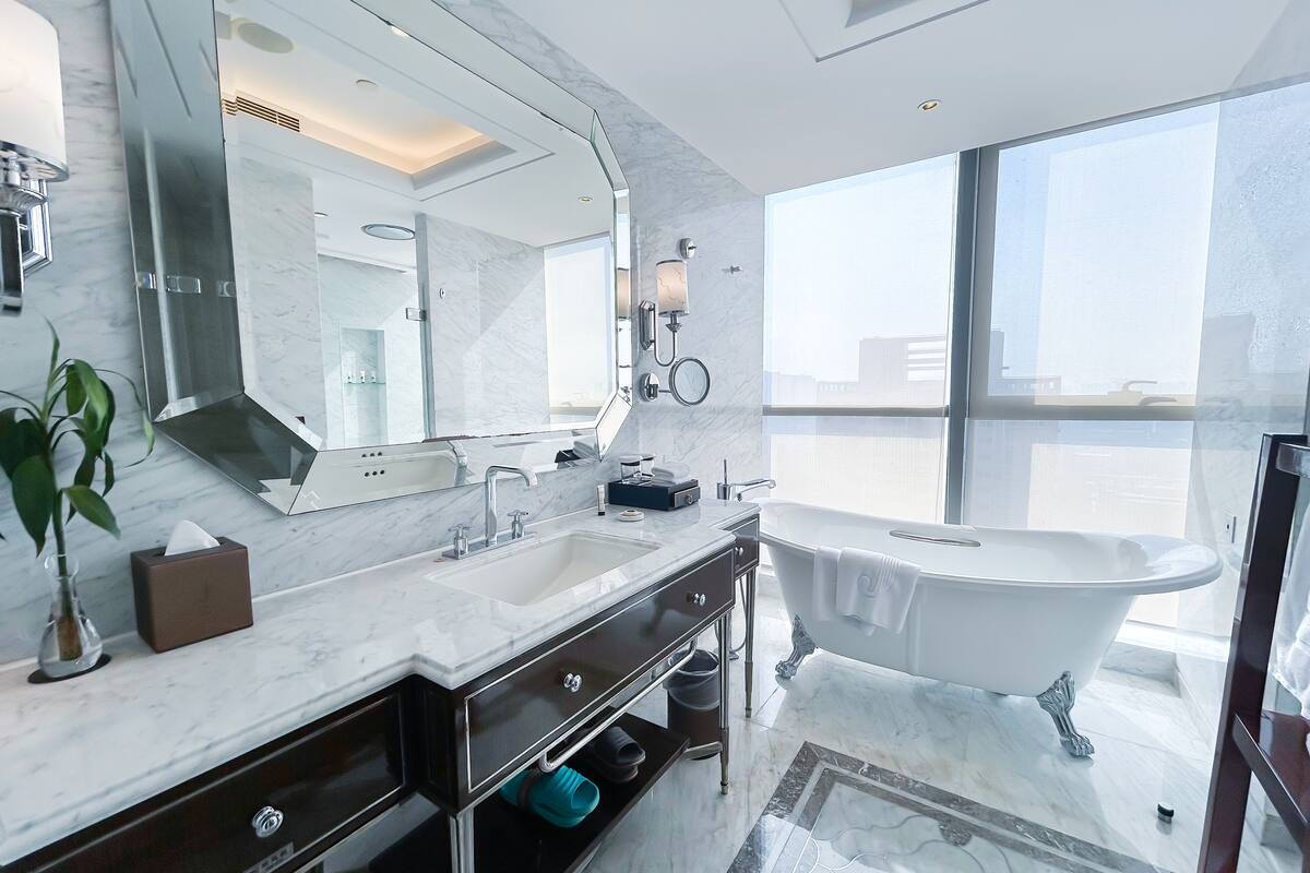 Une salle de bain moderne dotée d’un grand miroir, d’une baignoire sur pieds et d’une grande fenêtre offrant une vue sur la ville.