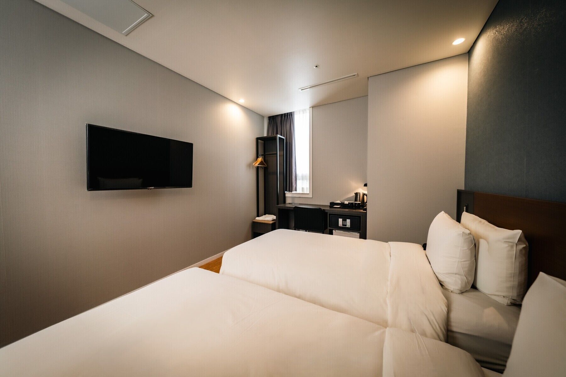 A hotel room with a bed, a desk, a chair, a TV, and a window with curtains.