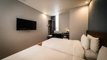 A hotel room with a bed, a desk, a chair, a TV, and a window with curtains.