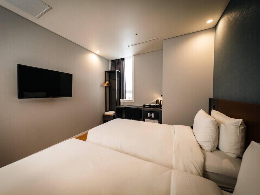 A hotel room with a bed, a desk, a chair, a TV, and a window with curtains.