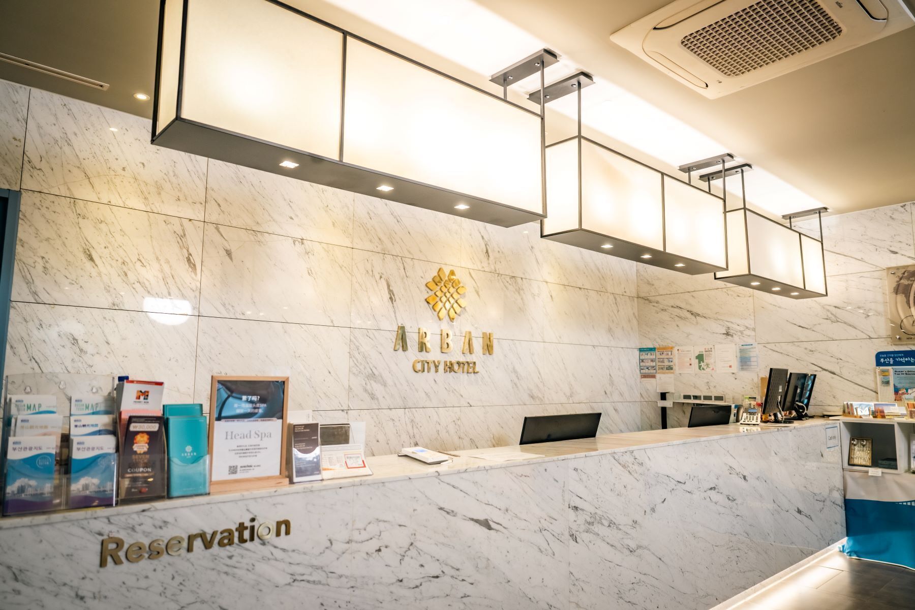 A hotel reception desk with a marble counter, a sign for the head spa, and various informational brochures.