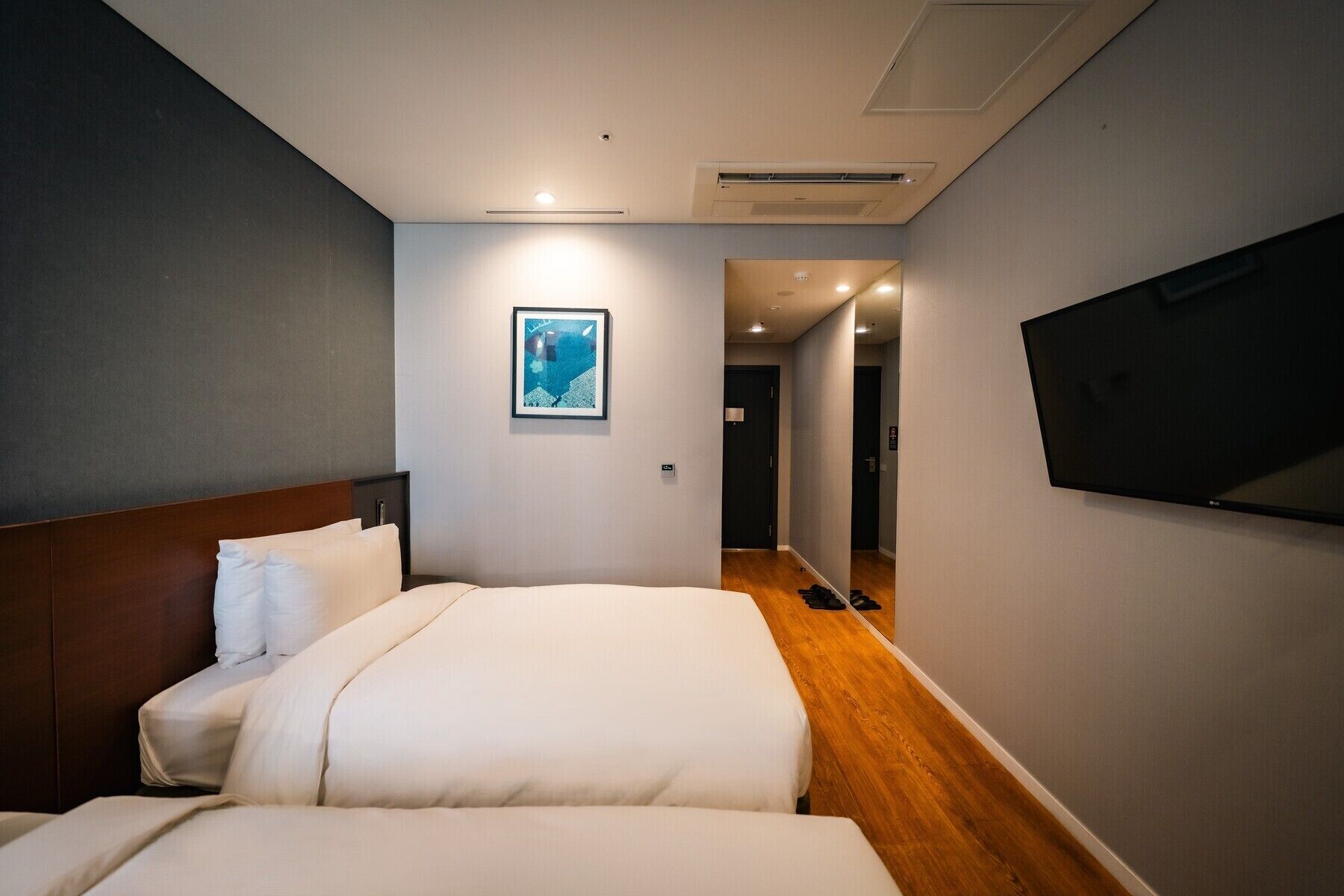A hotel room with two beds, a mounted TV, and a framed picture on the wall.