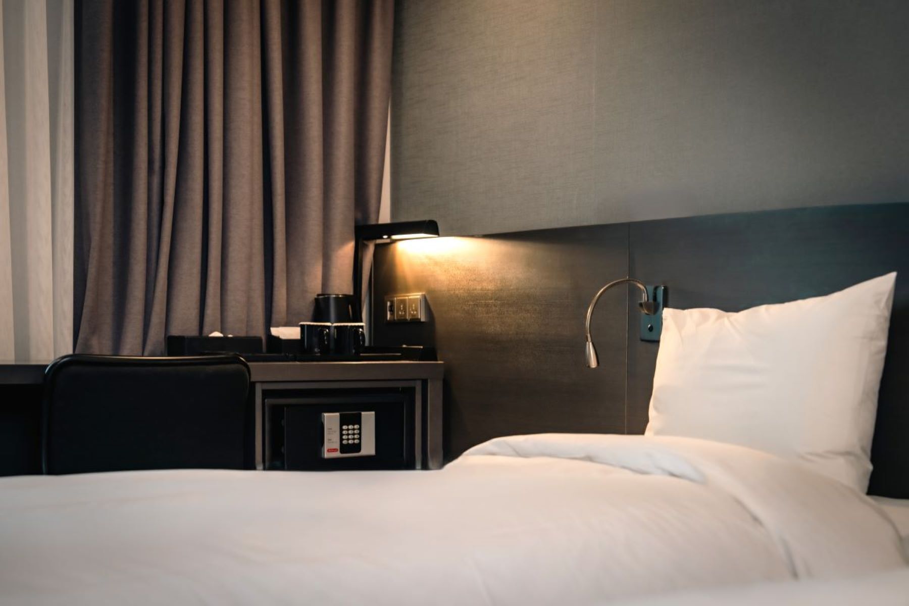 A hotel room with a bed, a nightstand with a coffee maker, a lamp, and a control panel.