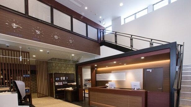 A hotel reception area with a wooden reception desk, a staircase, and clocks displaying times from London, Beijing, and New York. - Cabin & Lounge Highland Station Inn (Fujikawaguchiko)