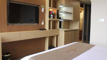 Ein Hotelzimmer mit Bett, einem an der Wand montierten Fernseher, einem Holzschrank und einer kleinen Ablage mit Blumen in einer Vase.