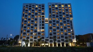 Um hotel moderno de vários andares, com janelas iluminadas e um elemento vertical central.