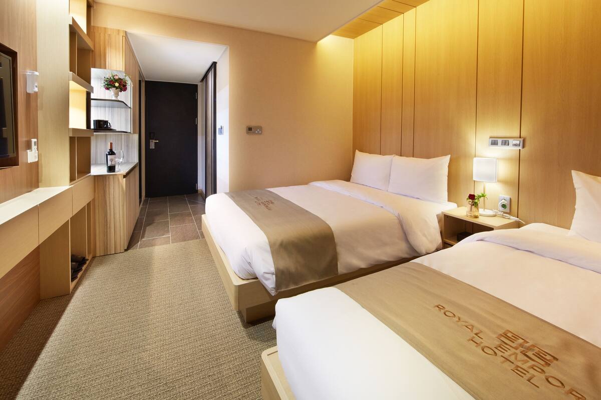 Une chambre d’hôtel avec deux lits, des boiseries, un minibar et une petite table sur laquelle est posé un vase.