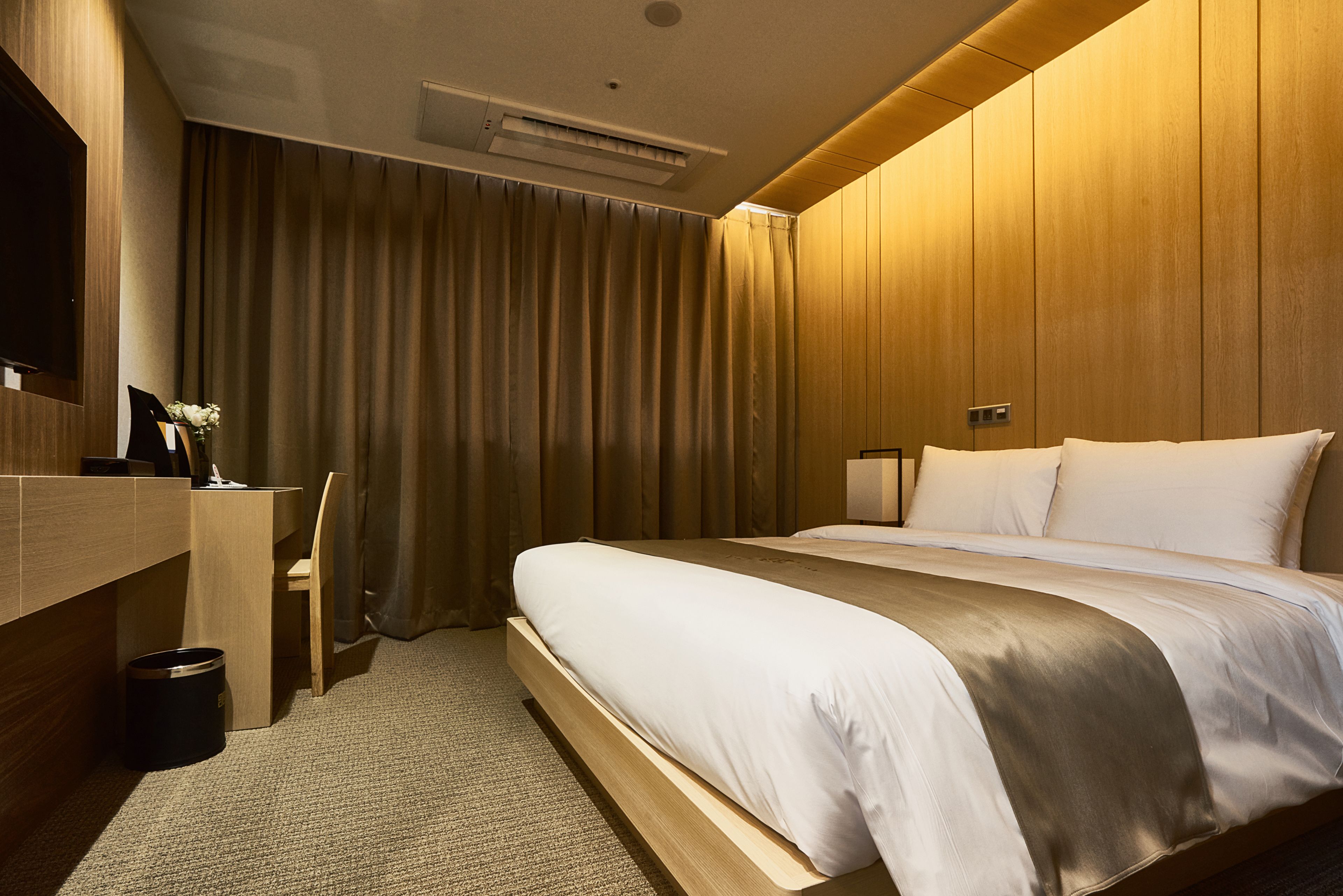 A hotel room with a wooden bed, a desk, a chair, and a television.