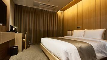 A hotel room with a wooden bed, a desk, a chair, and a television.