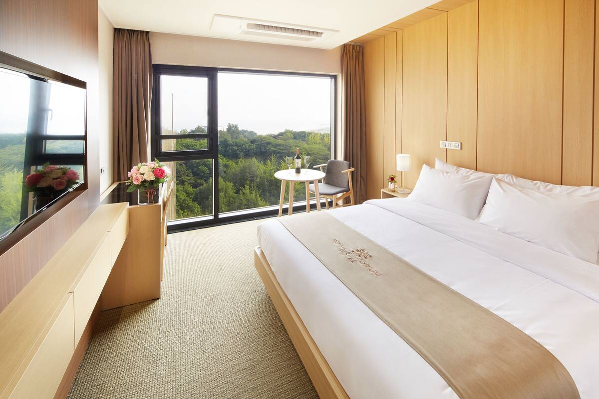 Une chambre d’hôtel dotée d’un grand lit, d’un bureau avec une chaise, d’une petite table avec une chaise et d’une grande fenêtre donnant sur l’extérieur.