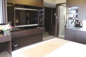 A modern hotel room with a large flat-screen TV, a wooden desk, and a small trash bin.
