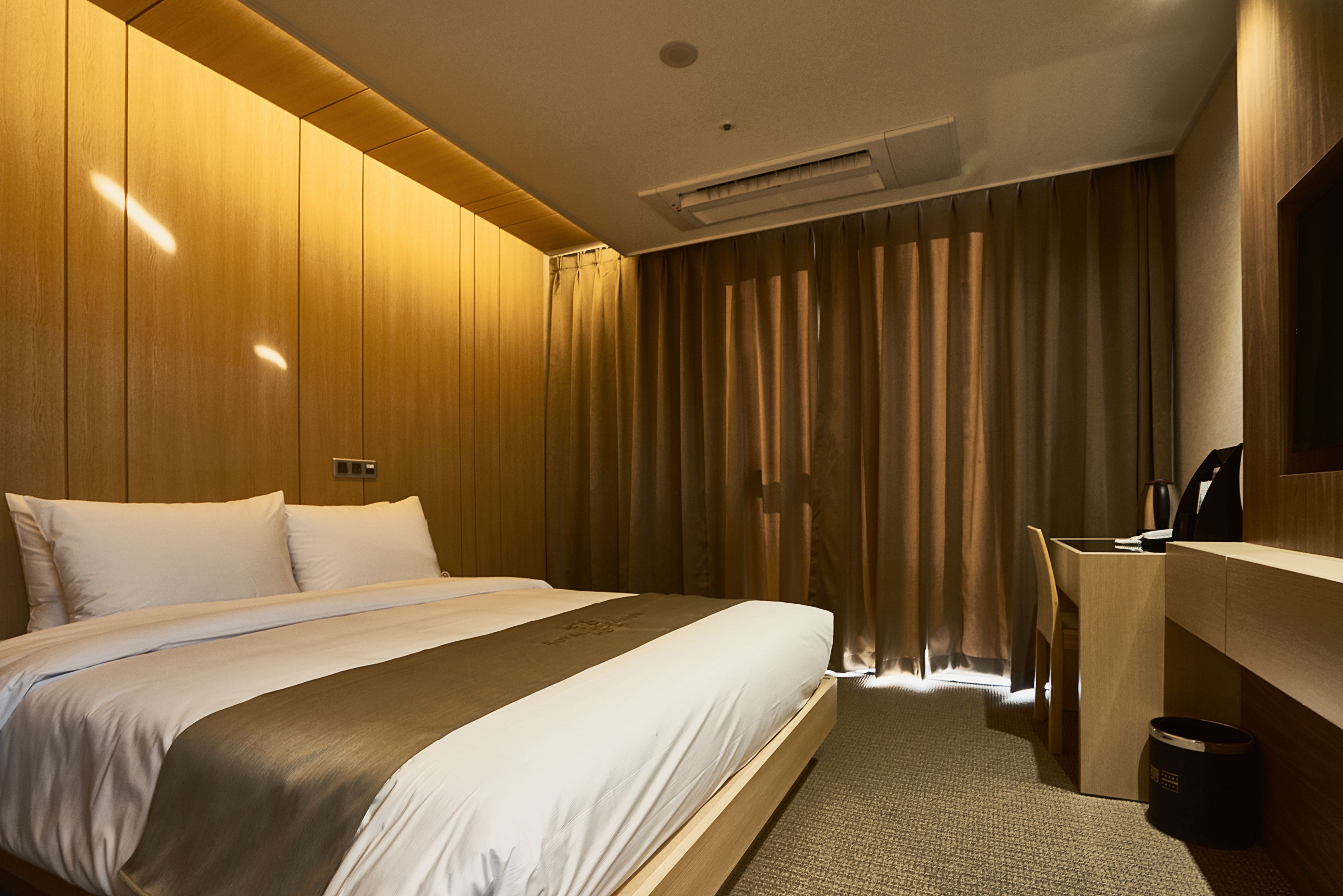 A hotel room with a large bed, wooden paneling, a desk, and a chair.