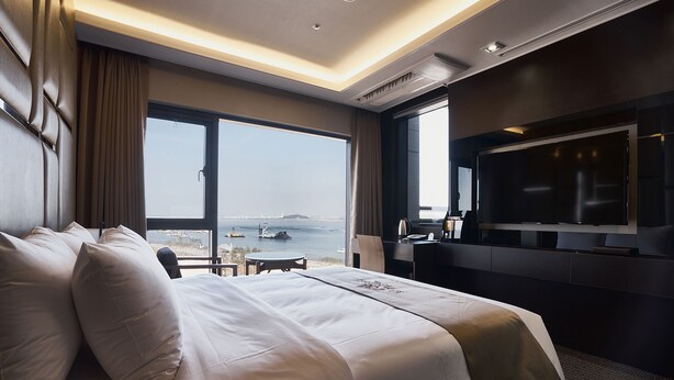 Quarto de hotel moderno com uma cama grande, uma mesa de escritório, televisão de tela plana e vista para o mar.