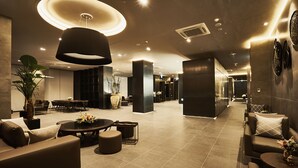 Um hall espaçoso com design moderno, apresentando uma grande área de estar, uma mesa de centro e uma luminária circular imponente.