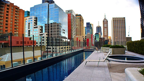 Una piscina en la azotea con vistas a la ciudad, rodeada de edificios modernos y un cielo despejado.
