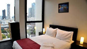 Habitación de hotel con una cama grande, una mesita de noche, una lámpara y vistas a la ciudad desde la ventana.