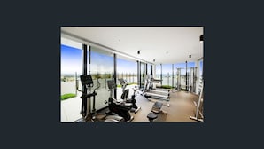 Un gimnasio moderno con diversos equipos de ejercicio, grandes ventanales y vistas a la ciudad.