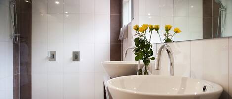 A modern bathroom with a large white sink, a mirror, and a shower area.