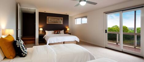 A hotel room with two beds, a ceiling fan, a large window with a view, and a door leading to a balcony.
