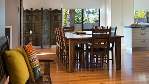 A dining area with a wooden table and chairs, a decorative partition, and a view of the outdoors. - Artemis Retreat (Daylesford)