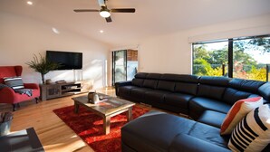 A modern living room with a black leather sofa, a red armchair, a wooden coffee table, and a red rug. - Artemis Retreat (Daylesford)