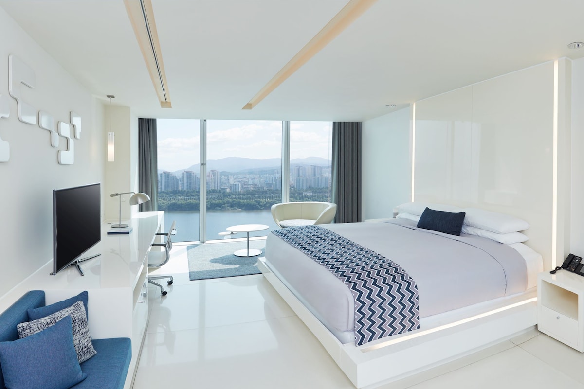 Une chambre moderne avec un grand lit, une télévision, un bureau et une vue sur la ville.