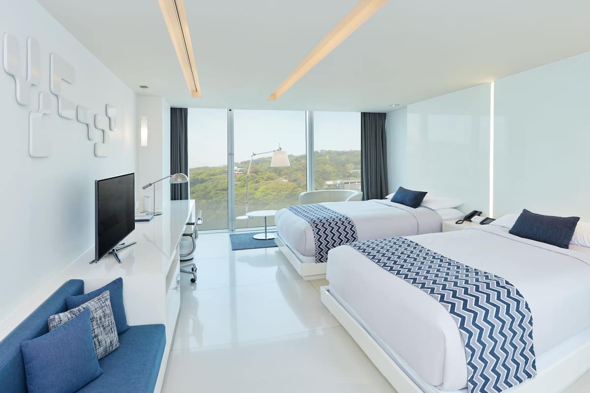 Een moderne hotelkamer met twee bedden, een televisie, een bureau en uitzicht op de stad.