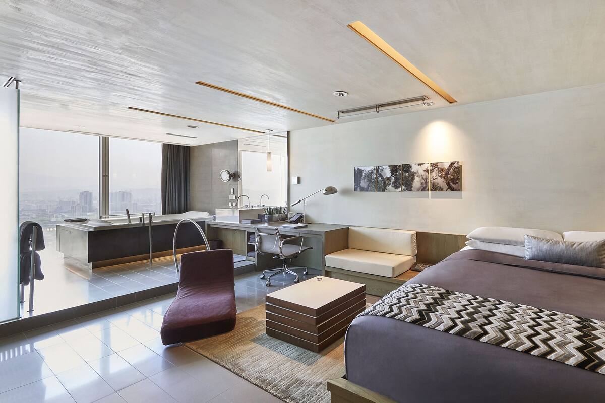Een moderne hotelkamer met een groot bed, een bureau, een stoel, een bank, een badkamer en uitzicht op de stad.