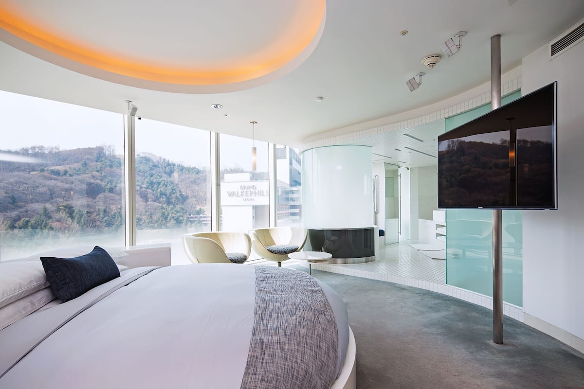 Een moderne hotelkamer met een groot bed, een flatscreen televisie en uitzicht op een bergachtig landschap.
