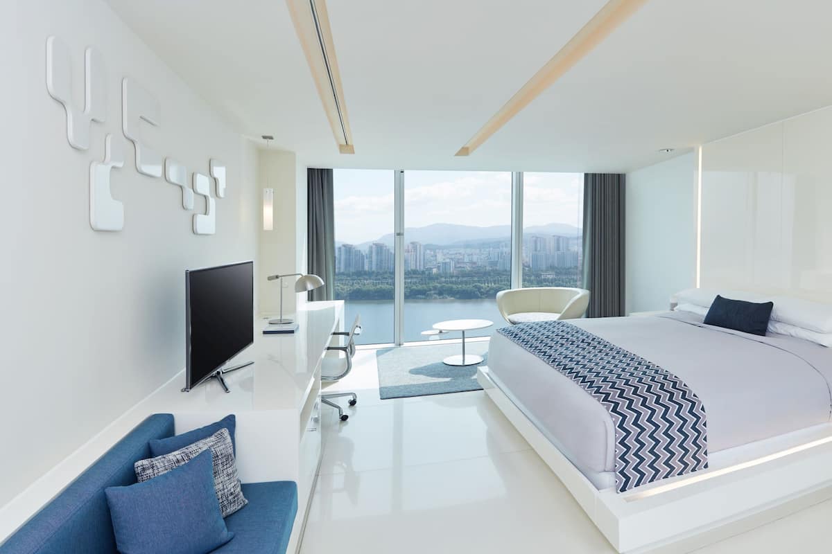 Een moderne slaapkamer met een groot bed, een televisie, een bureau en uitzicht op de stad.